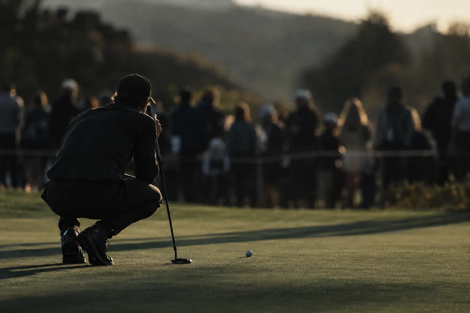 A golfer crouched behind a ball reading a putt, with a blurred gallery behind.
